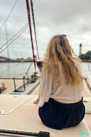 The writer of the post with long blonde hair sits on a boat, facing the water. A lighthouse and cloudy sky are visible in the background.