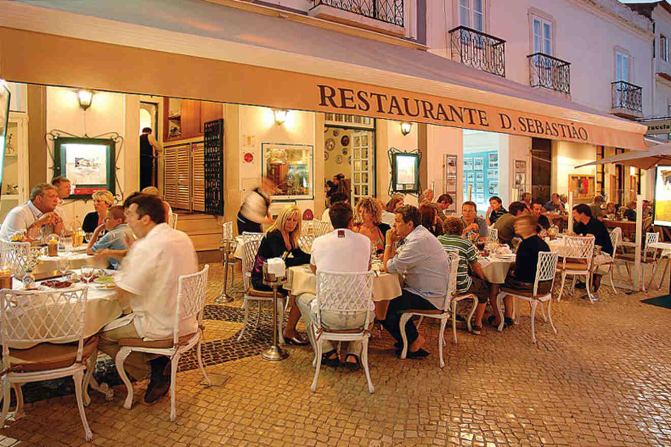 People dining at outdoor tables in front of Restaurante D. Sebastião, under a lit awning in evening light.