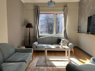 Living room with gray sofas, a wooden floor, a coffee table, a tall lamp, and a large window with a view of trees.