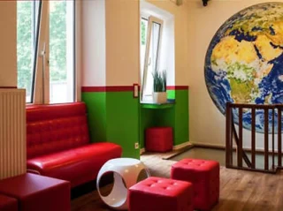 Room with red seating, green and white walls, a large globe mural, wooden floor, and windows with plants.