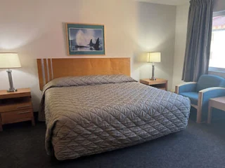 Hotel room with a single large bed, two bedside tables with lamps, an armchair, and a framed picture on the wall.