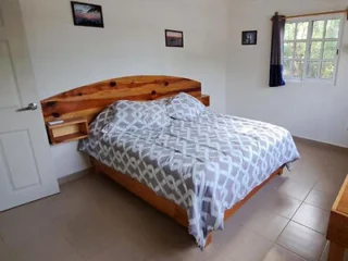 A neatly made bed with a patterned gray and white comforter in a simple bedroom with framed pictures on the walls and a window.