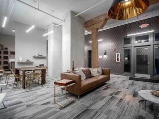 A modern lobby with a brown sofa, a table with chairs, geometric-patterned carpet, and a large gold pendant light.