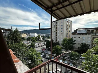View from a balcony overlooking a parking lot, apartment buildings, and a distant hilly landscape under a cloudy sky.