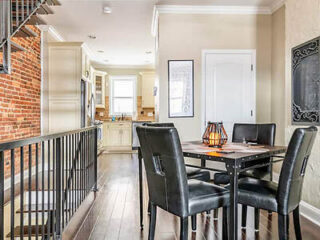 Dining area with a black table and four chairs, adjacent to a kitchen. Exposed brick wall on the left and a decorative candle holder on the table.