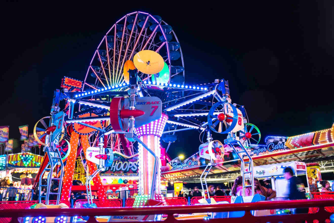 A brightly lit carnival at night featuring an illuminated Ferris wheel and colorful rides, with people enjoying the attractions.