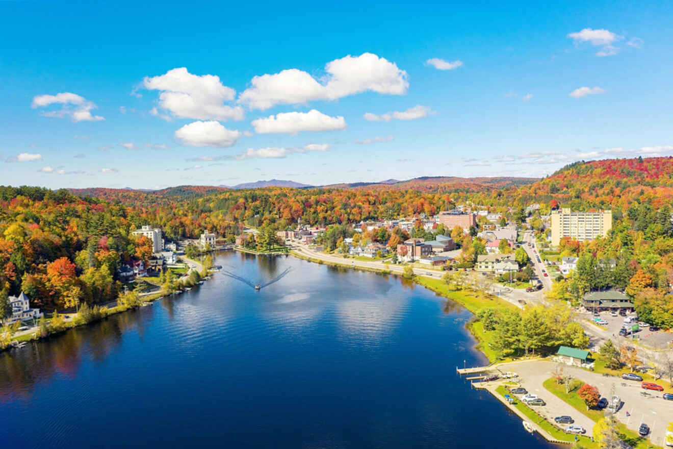 Aerial view of a town beside a river surrounded by colorful autumn trees, under a clear blue sky.