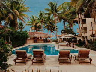 A tranquil poolside scene with lounge chairs, a bar area, and palm trees under a clear sky.