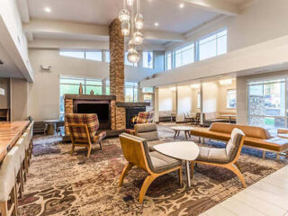 Spacious lobby with modern furniture, including chairs and sofas, a stone fireplace, hanging lights, and large windows providing natural light.