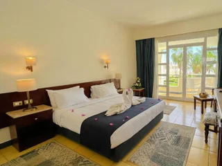 Hotel room with a double bed, bedside tables, lamps, and a window overlooking a garden. Towels folded into swans are on the bed.