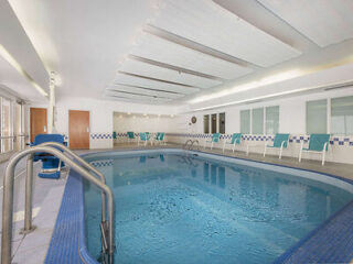 Indoor swimming pool with blue tiles, lounge chairs, and a handrail. Ceiling features white panels and fluorescent lighting.