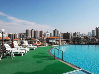 Rooftop pool with lounge chairs overlooking a cityscape with tall buildings under a clear blue sky.