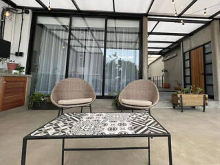 Patio with two wicker chairs and a patterned metal table in front of a glass wall and door.