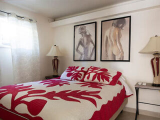 Bedroom with a red and white bedspread, two lamps, and two framed artworks of figures on the wall.