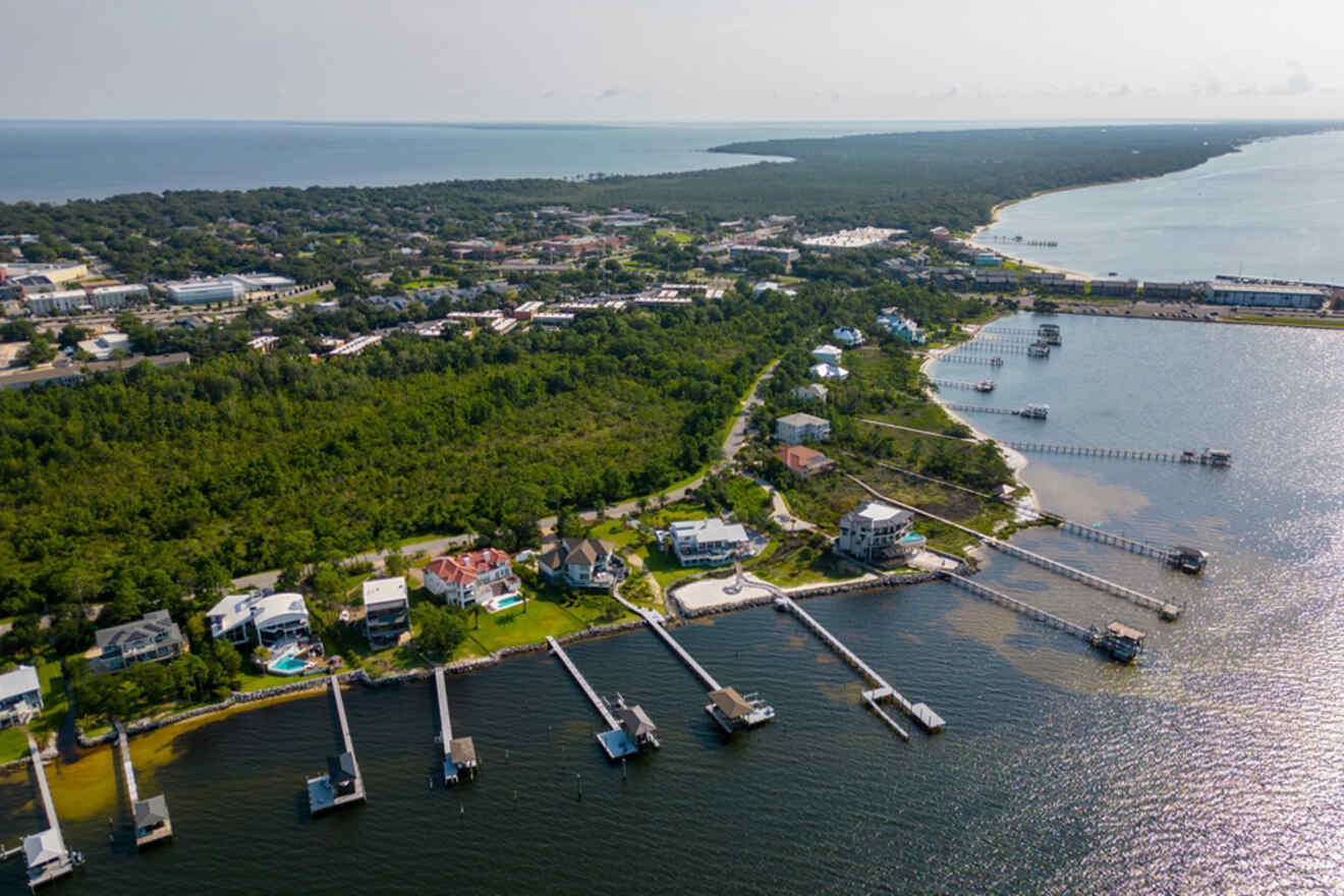 Aerial view of a coastal town with houses, piers extending into the water, and a forested area in the background.