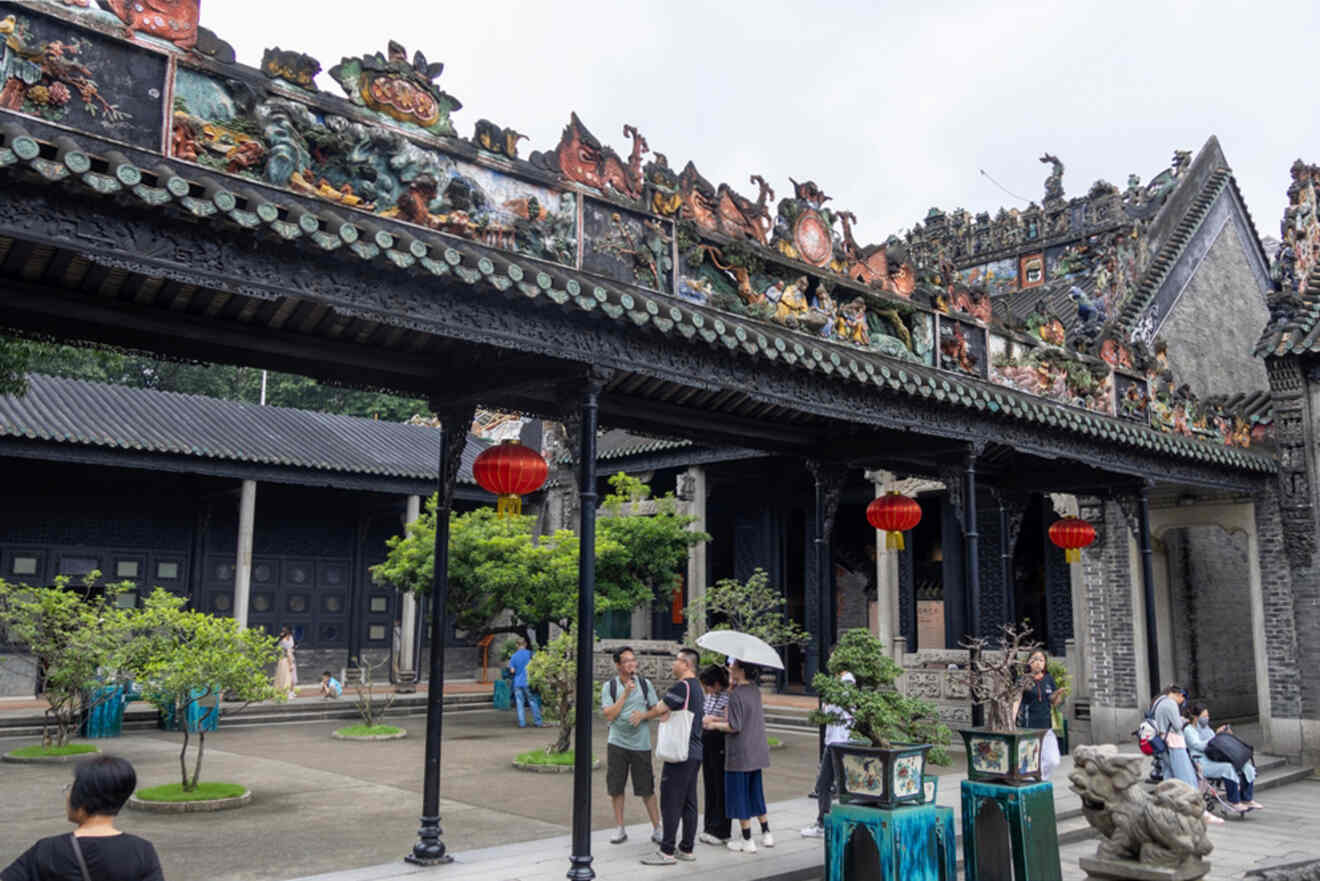 Visitors explore a traditional Chinese courtyard adorned with decorative roof sculptures and red lanterns.