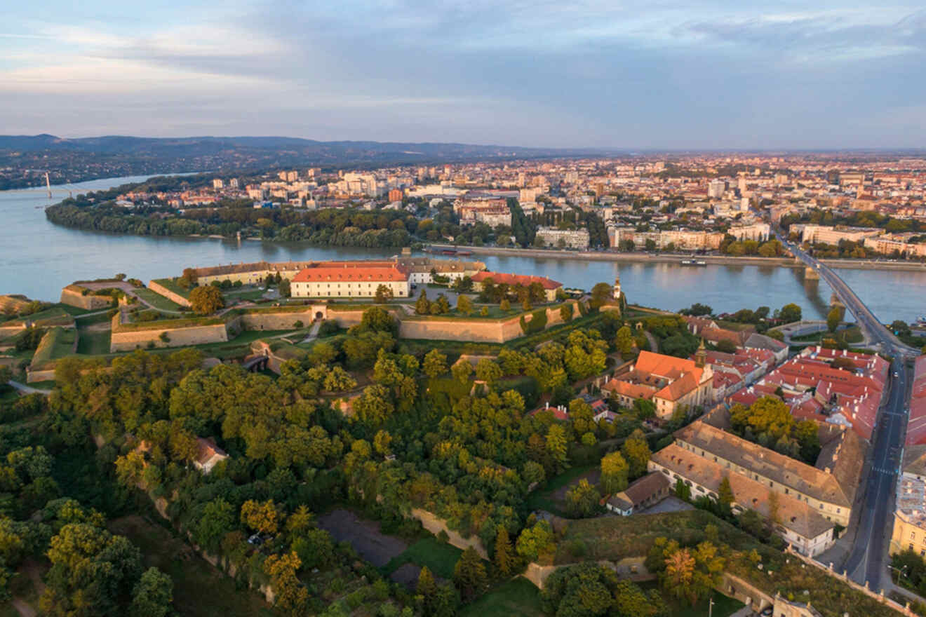 Aerial view of a historical fortress surrounded by greenery with a city and river in the background under a clear sky.