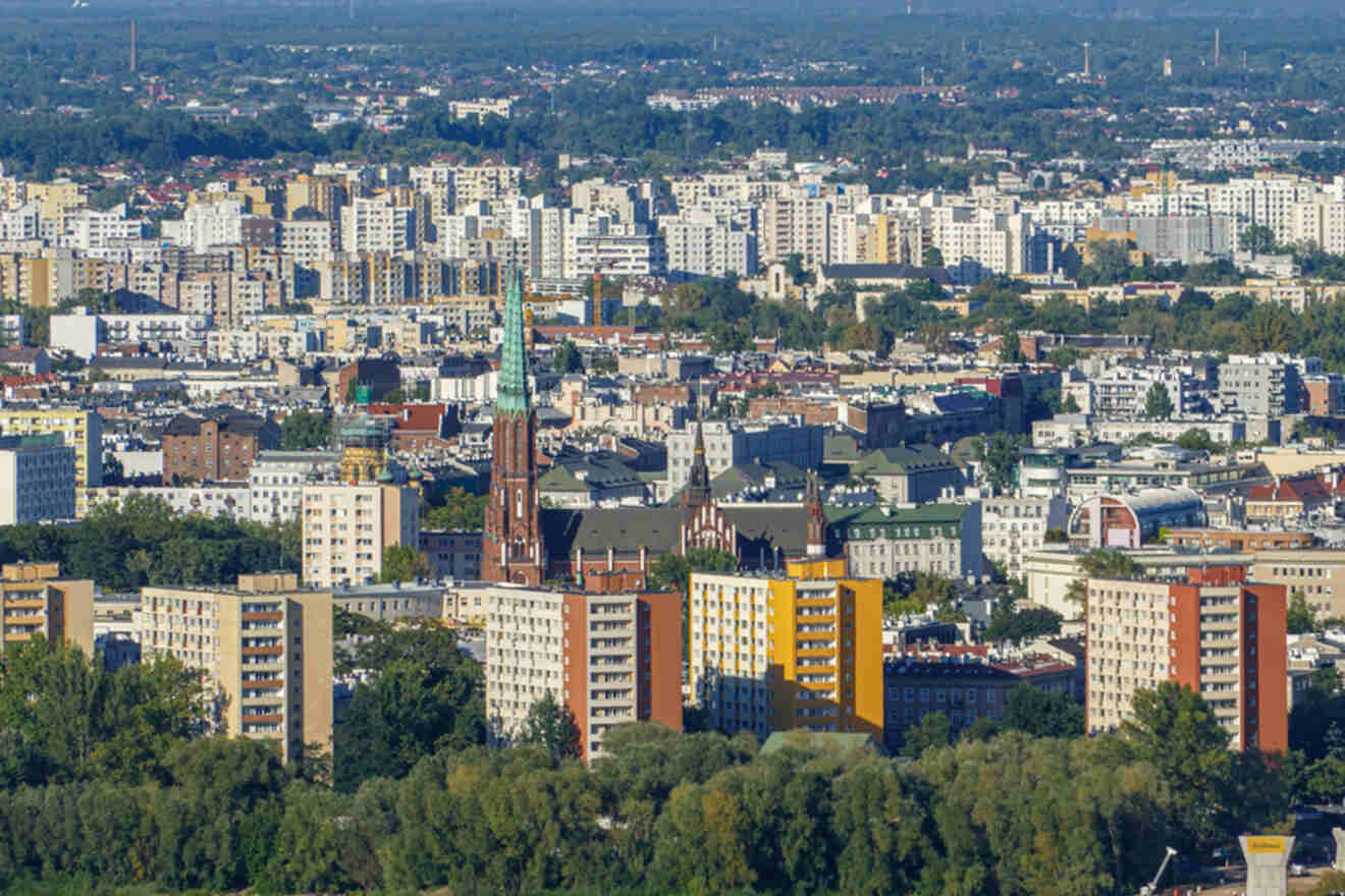 Aerial view of Warsaw's Praga district with a mix of residential buildings, a visible church spire, and green treetops in the foreground.