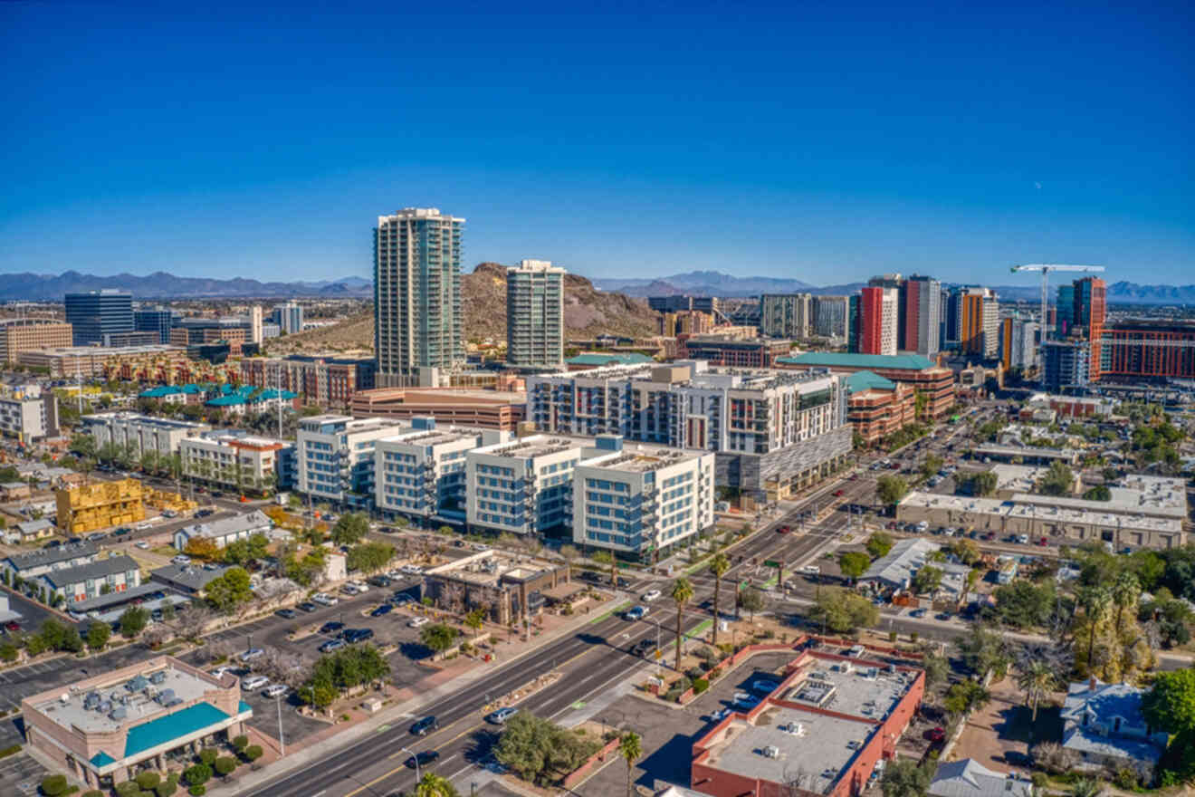 Aerial view of a cityscape with modern high-rise buildings, streets, and residential areas under a clear blue sky.