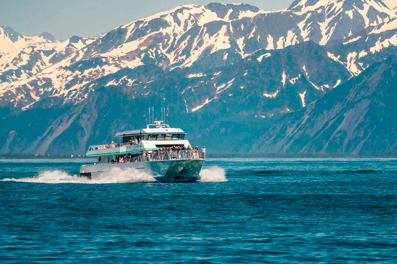 A boat travels on a body of water with snow-capped mountains in the background.