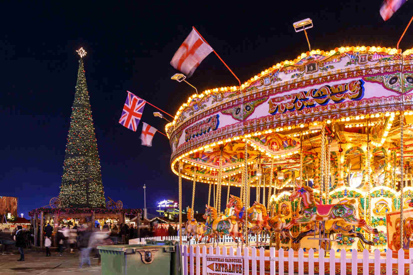 A brightly lit carousel with colorful decorations sits next to a large Christmas tree adorned with lights. Flags flutter above the carousel on a bustling night.