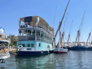 A two-story boat with a covered deck is docked alongside several other boats under a clear blue sky.