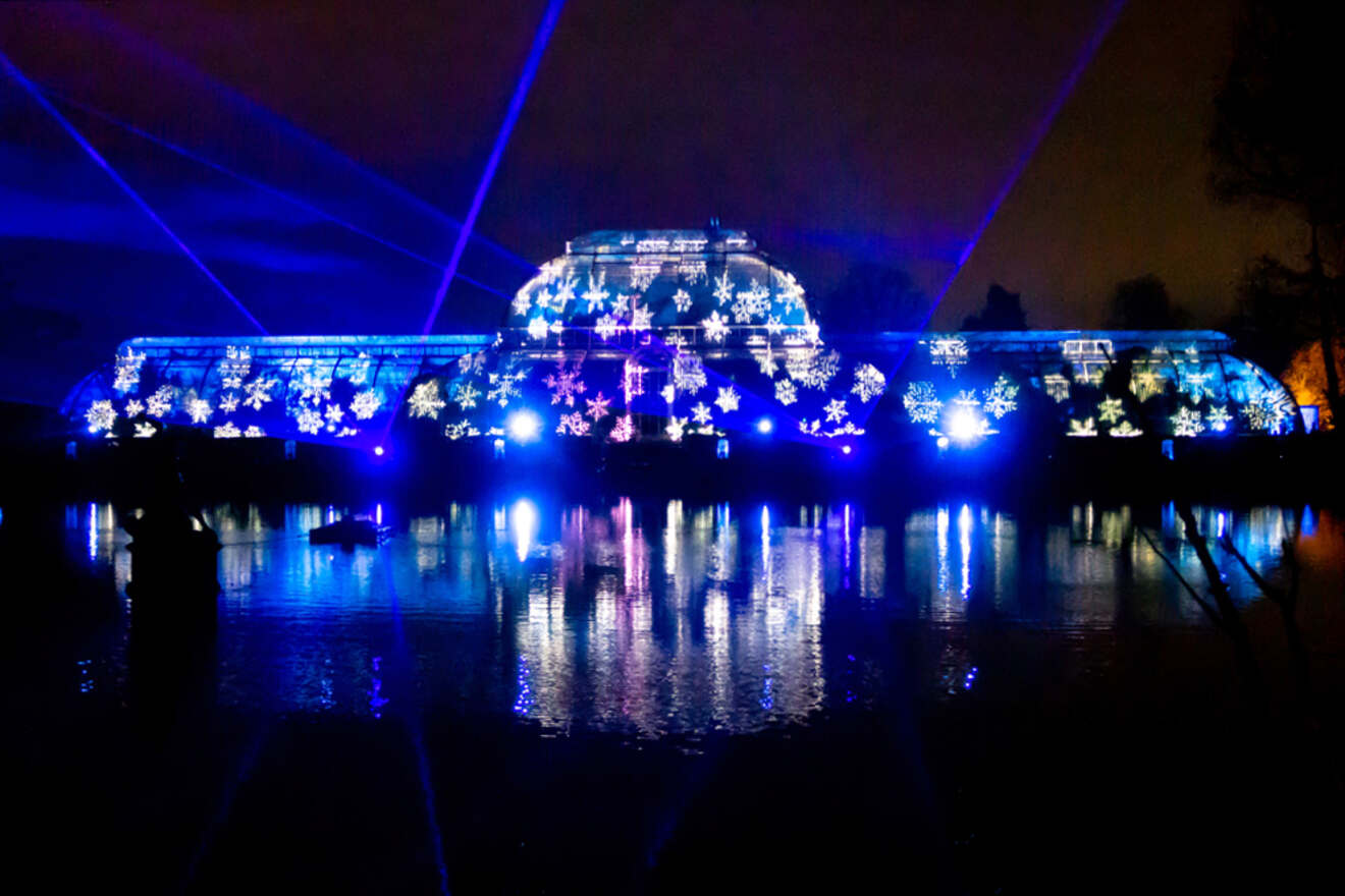 A brightly lit structure with blue and white star patterns is reflected in a body of water at night.