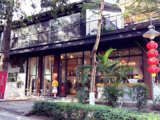 Exterior view of a two-story modern building with large glass windows. Plants and lanterns decorate the entrance, and there is a figurine outside.