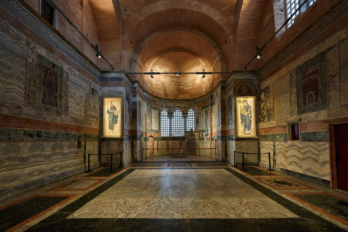 Interior of a Byzantine-style building with high arched ceilings, decorative walls, and framed religious art. Natural light filters through a large central window.