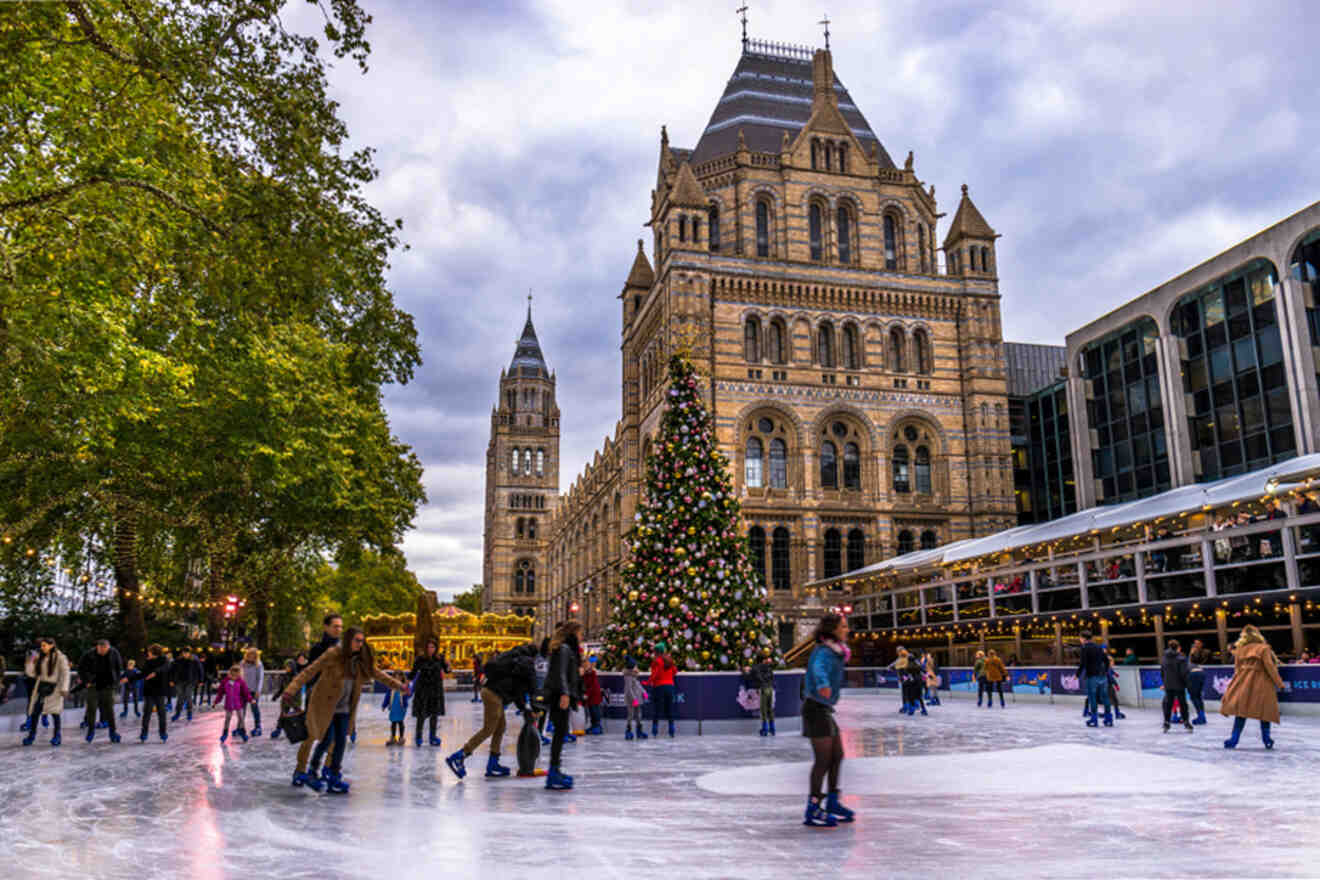 People ice skating in front of a historic building with a large decorated Christmas tree nearby, under a cloudy sky.