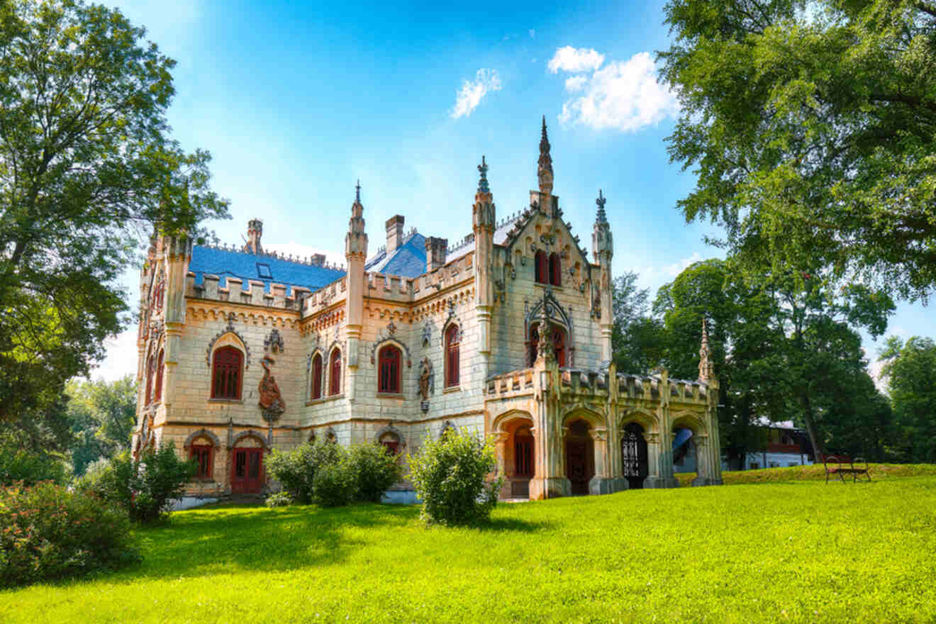 A historic Gothic-style castle surrounded by green grass and trees under a blue sky.