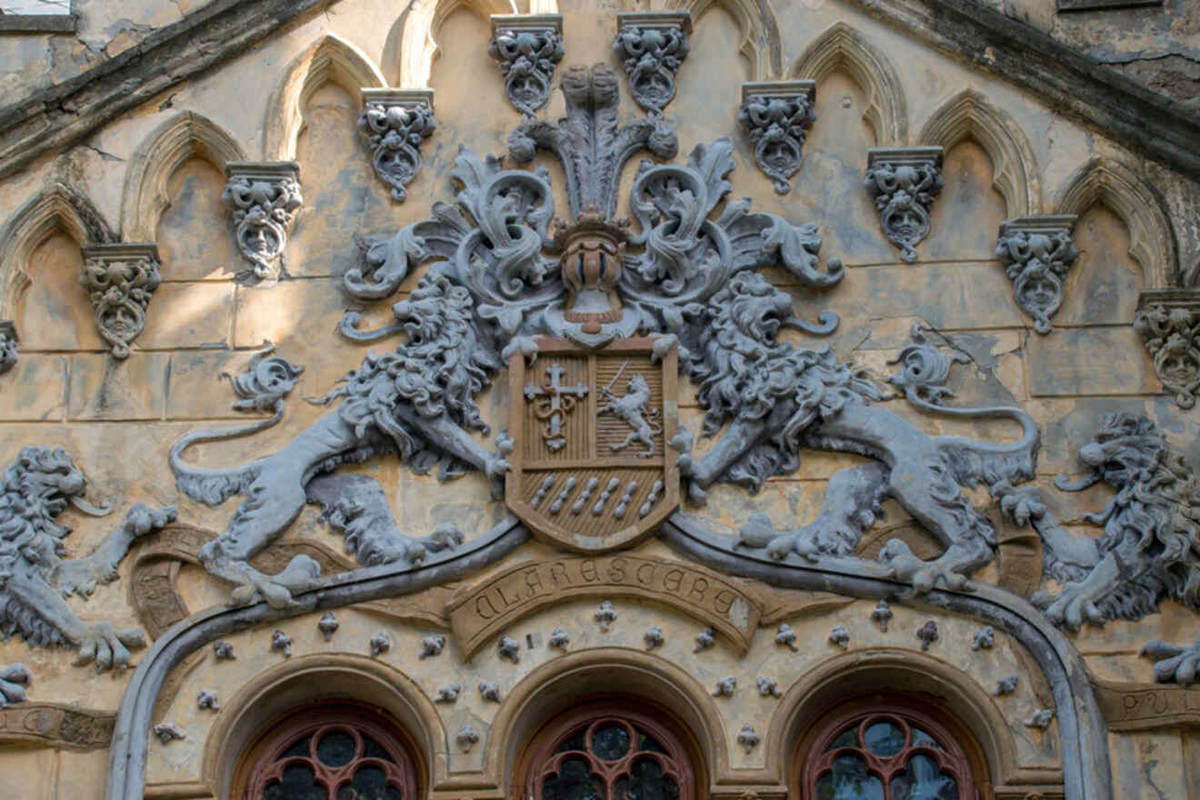 Stone carving of a crest with two lions flanking a shield, topped by a crown, on an ornate building facade with decorative arches.