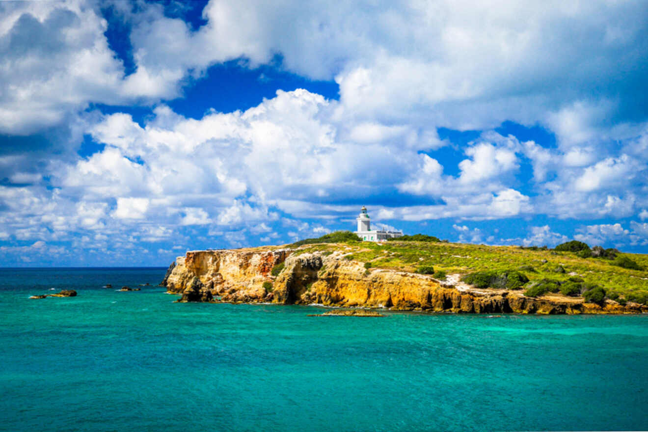 A lighthouse sits atop a rocky cliff surrounded by turquoise sea under a partly cloudy sky.