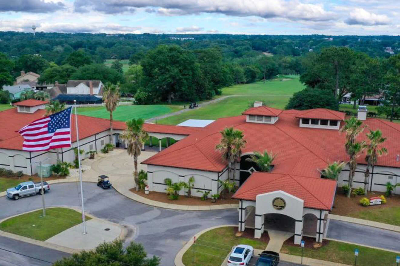 Aerial view of a building with red roofs surrounded by greenery, an American flag, and several vehicles in the parking area.