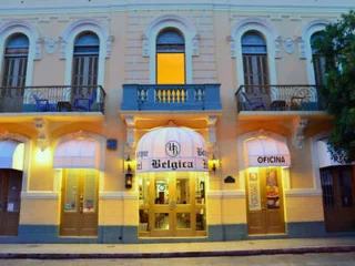 A historic building facade with arched windows and balconies. The entrance has an awning labeled "Belgica" and adjacent doors marked "Oficina.