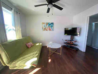 Living room with a green futon, round white coffee table, mounted TV, wall art, ceiling fan, and wood flooring.