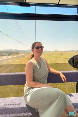 author of the post in sunglasses sits inside a cable car, enjoying the scenic vistas of grassy fields and distant hills—a perfect moment on their Serbia itinerary.