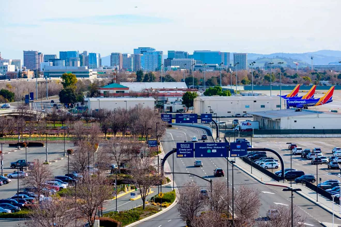 View of a busy street leading to an airport with planes parked in the distance and a city skyline in the background.