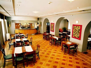 Empty restaurant interior with wooden tables and chairs, a bar counter in the background, and framed artwork on the walls.