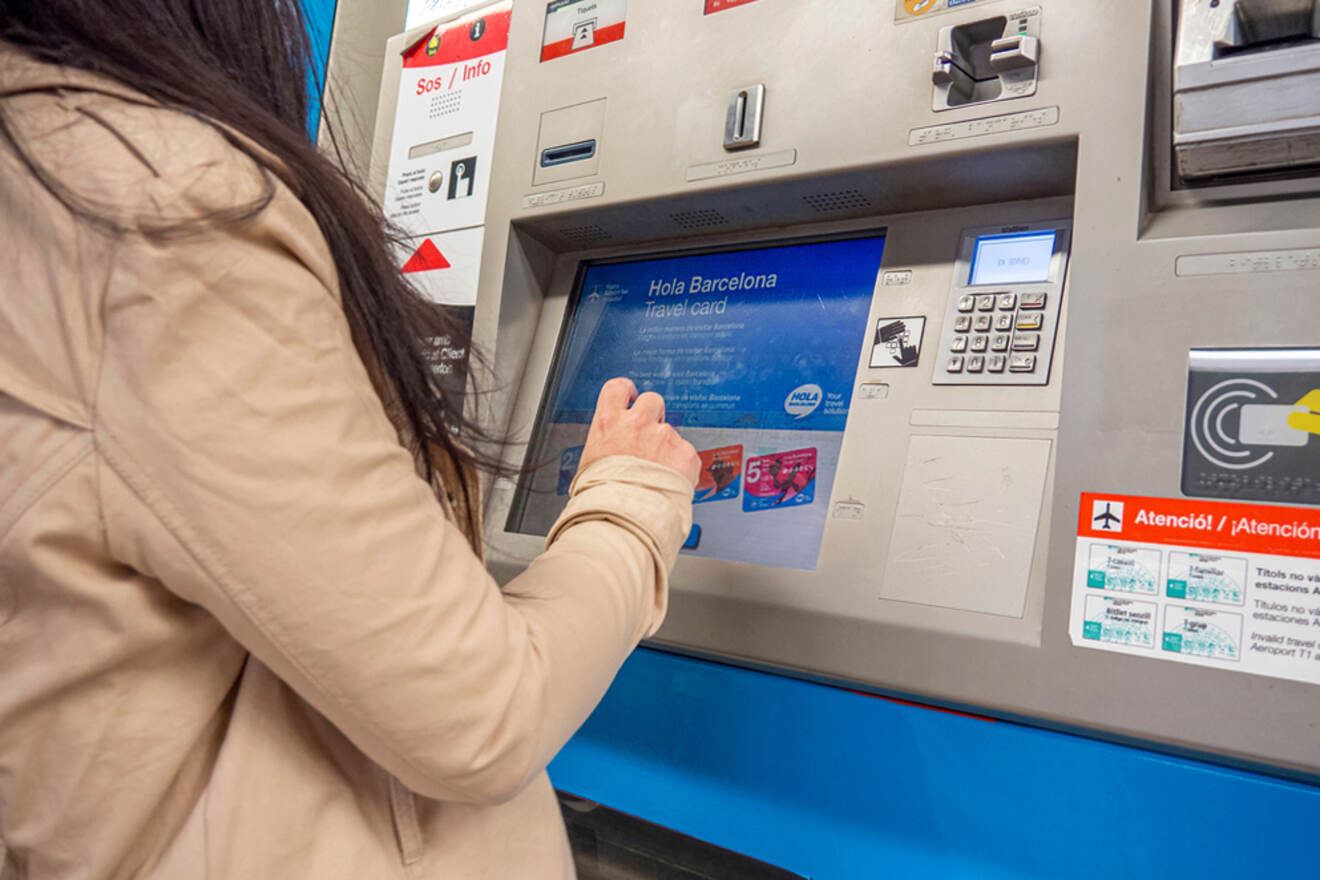 A person uses a ticket vending machine at a train station in Barcelona.