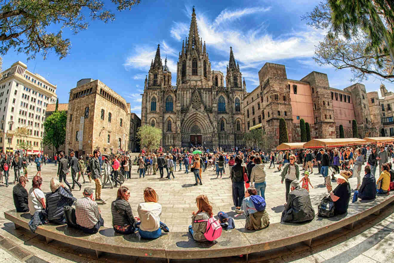 People gather in a plaza in front of a large Gothic cathedral with spires and intricate architecture, surrounded by historic buildings.