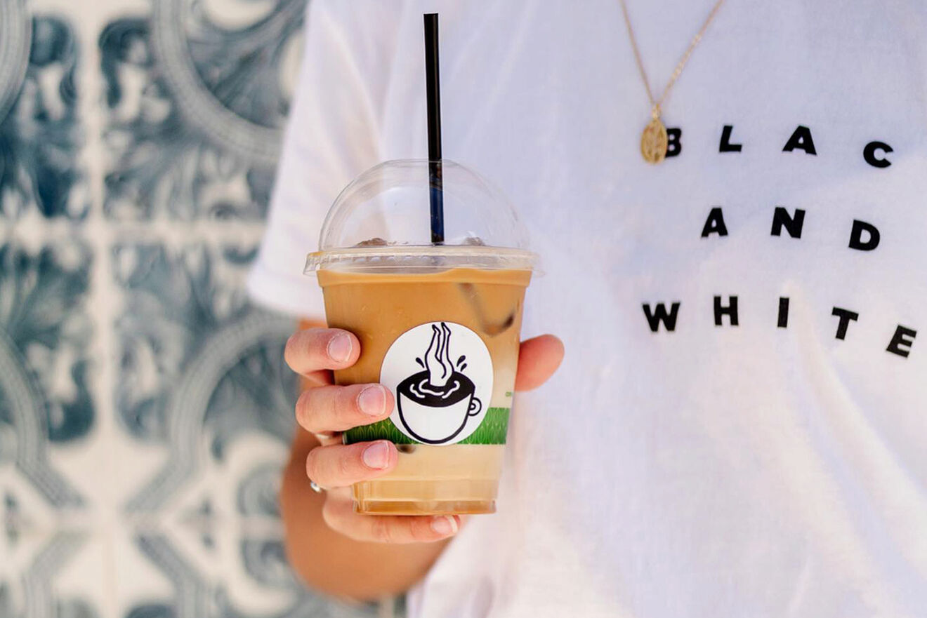 Person holding an iced coffee with a black straw, wearing a white shirt with "BLACK AND WHITE" text.