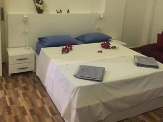 A neatly made bed with white linens, two blue pillows, and decorative flowers on top. Two towels are placed at the foot of the bed, and a small nightstand is on the side.