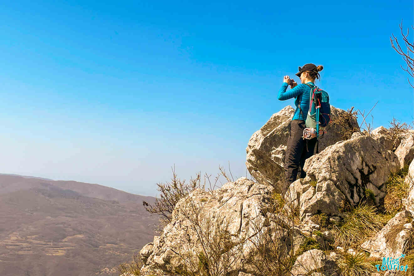 A person stands on rocky terrain, capturing the stunning Serbian mountainscape, their backpack and outdoor gear ready for the next leg of their Serbia itinerary beneath a clear blue sky.