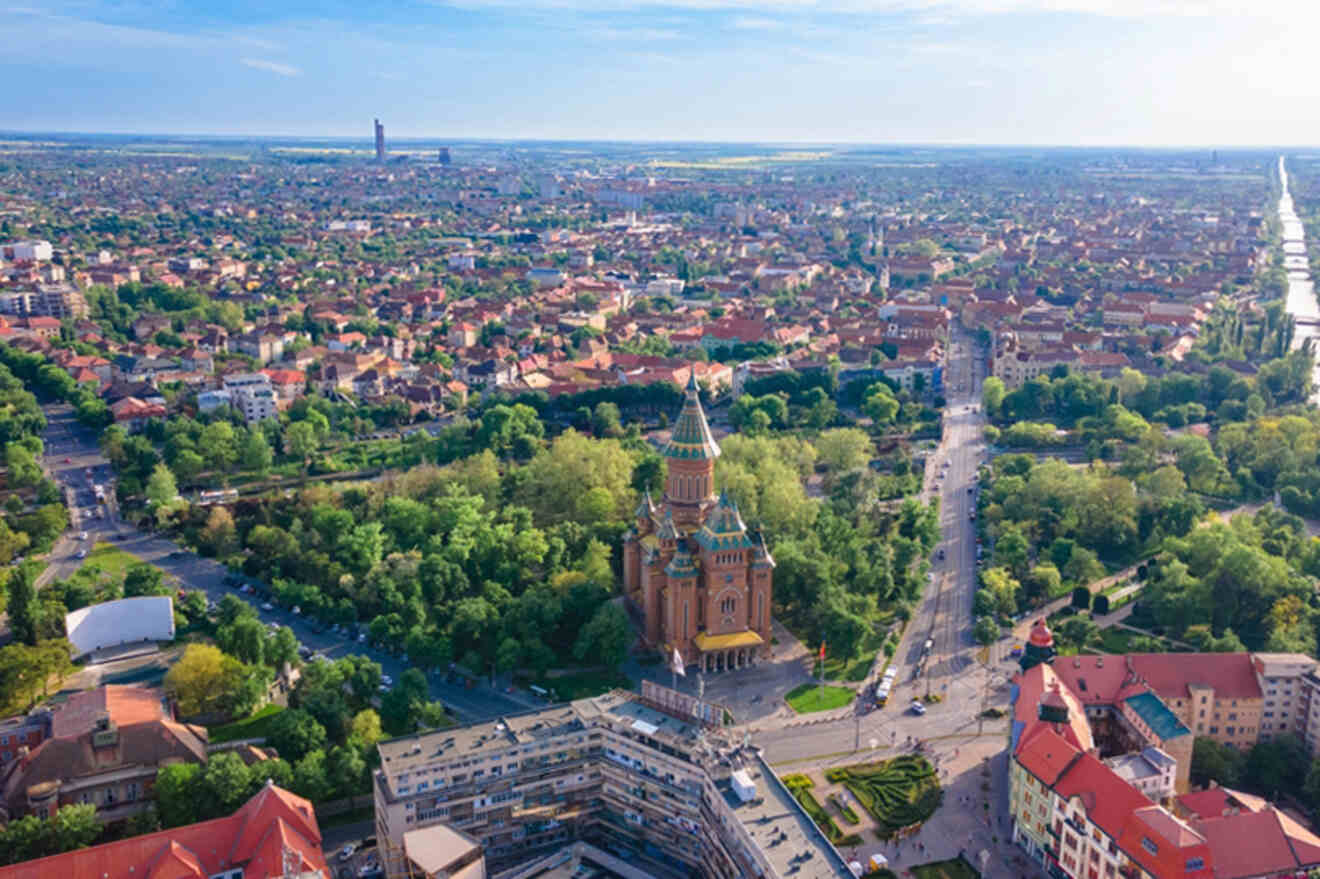 Aerial view of a city with a prominent ornate building surrounded by trees, intersecting roads, and numerous houses spread across the landscape.