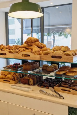 Bakery display with croissants, breads, pastries, and desserts arranged on shelves under a hanging lamp.