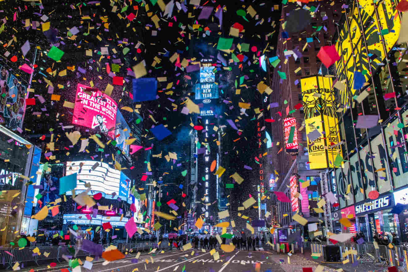 Times Square lit up at night with colorful confetti falling from above, surrounded by bright billboards and signs.