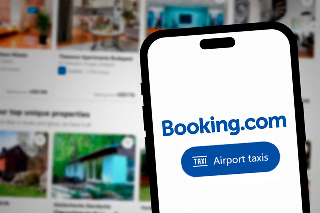 Smartphone showing Booking.com app, with background displaying various accommodation options.