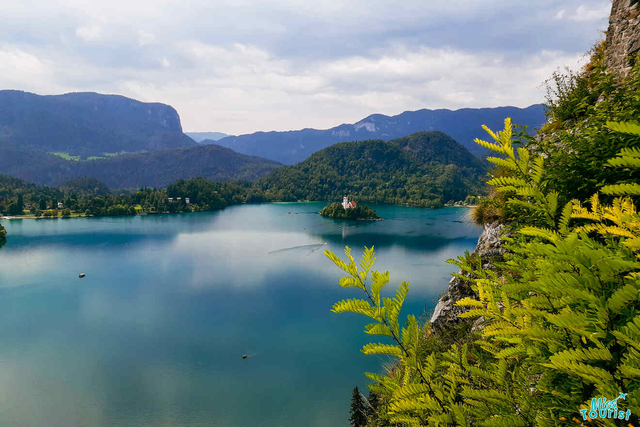 A scenic view of Lake Bled with a small island and church in the center, surrounded by mountains and greenery.