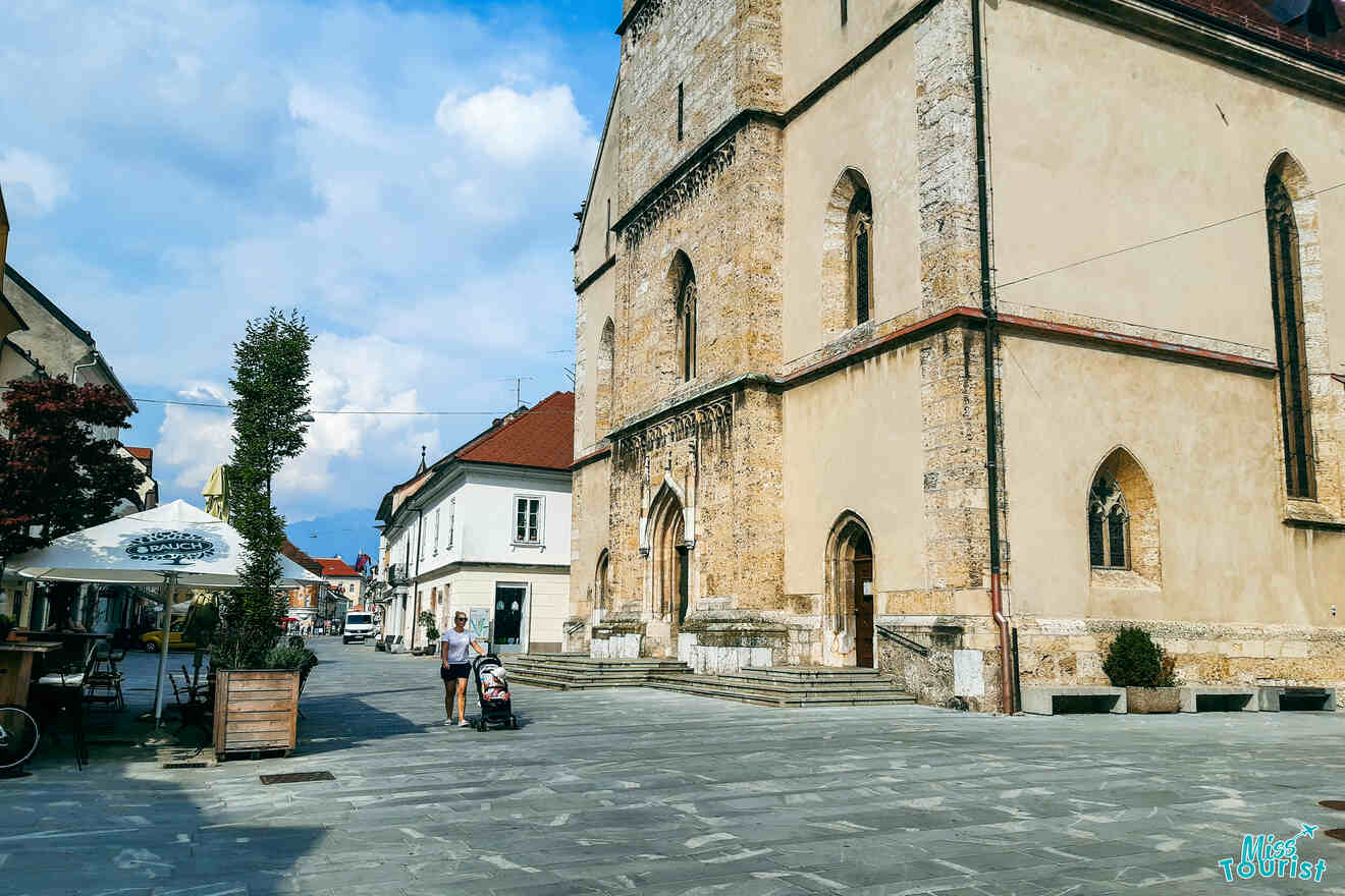 A historic stone church on a quiet cobblestone street with a few outdoor café tables and people walking nearby.